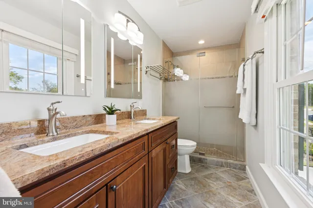 a bathroom with a granite countertop sink a toilet a mirror and shower