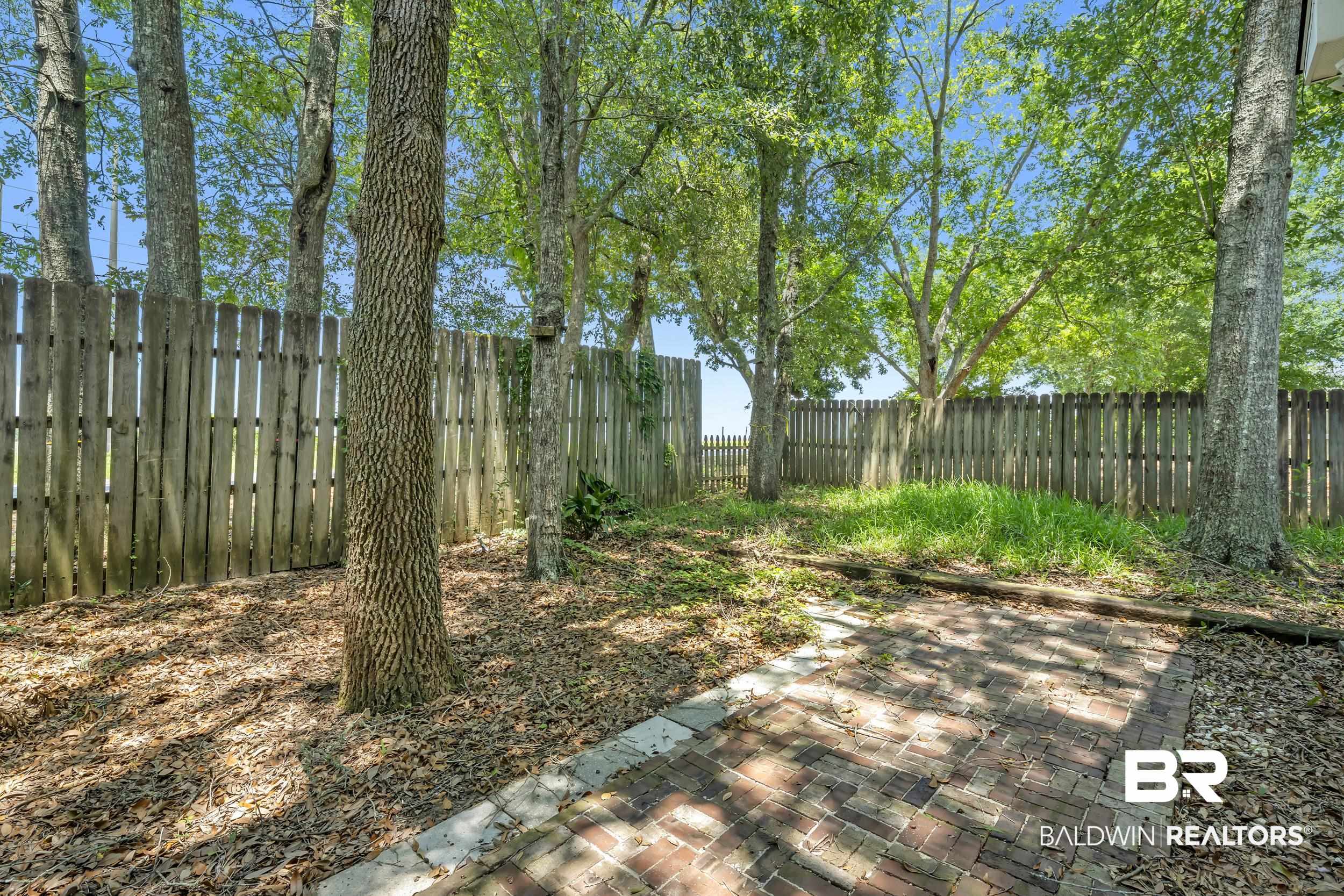 17488 Pandion Ridge, Unit A1 Fairhope, AL 36532 - Photo 17 of 18 Outdoor space featuring a brick paver patio, wood privacy fencing, and mature trees providing natural shade