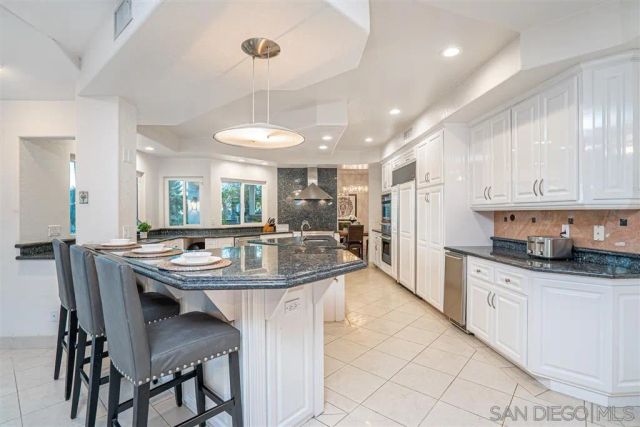 a kitchen with stainless steel appliances kitchen island granite countertop a dining table chairs and white cabinets