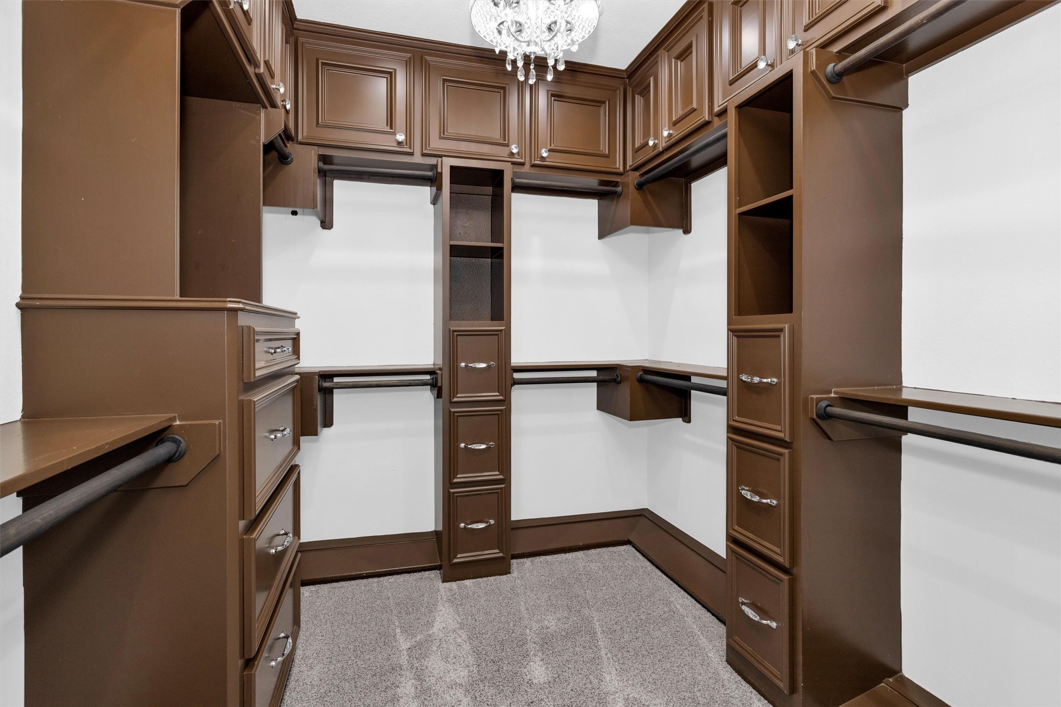10887 Decatur Street Willis, TX 77318 - Photo 31 of 50 The second custom primary walk-in closet with rich built-ins featuring extensive hanging space, drawer storage, and upper cabinetry—finished with its own chandelier for a polished, boutique-style feel.