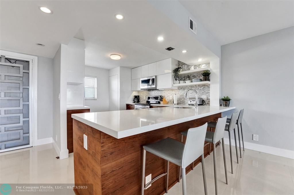 a kitchen with stainless steel appliances kitchen island granite countertop a sink a stove a refrigerator and white cabinets with wooden floor