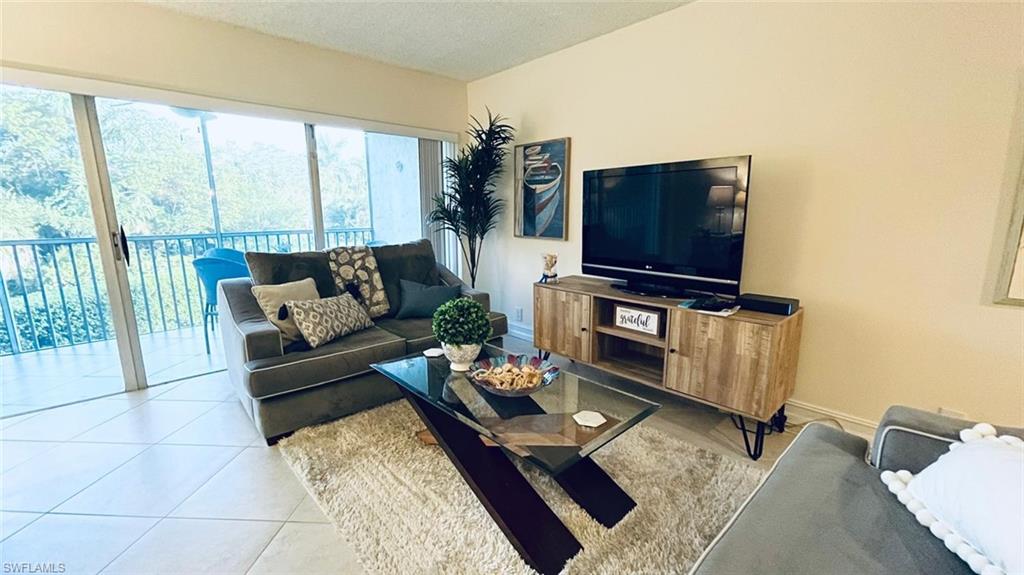 1 Bluebill Avenue, Unit 210 Naples, FL 34108 - Photo 11 of 17 a living room with furniture a flat screen tv and a floor to ceiling window