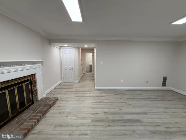 a view of an empty room with wooden floor fireplace and a window