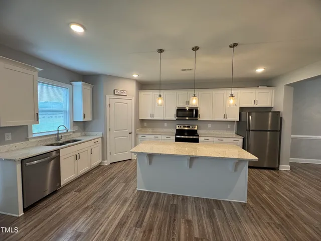 a large kitchen with stainless steel appliances a large counter top a stove a sink dishwasher a refrigerator and white cabinets with wooden floor