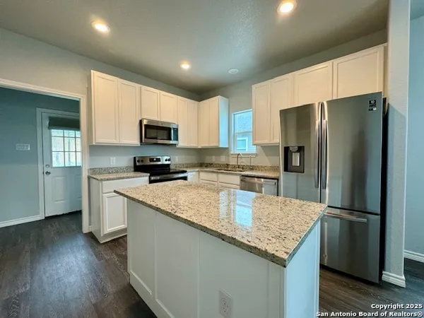 a kitchen with granite countertop a refrigerator a sink a stove a microwave and island