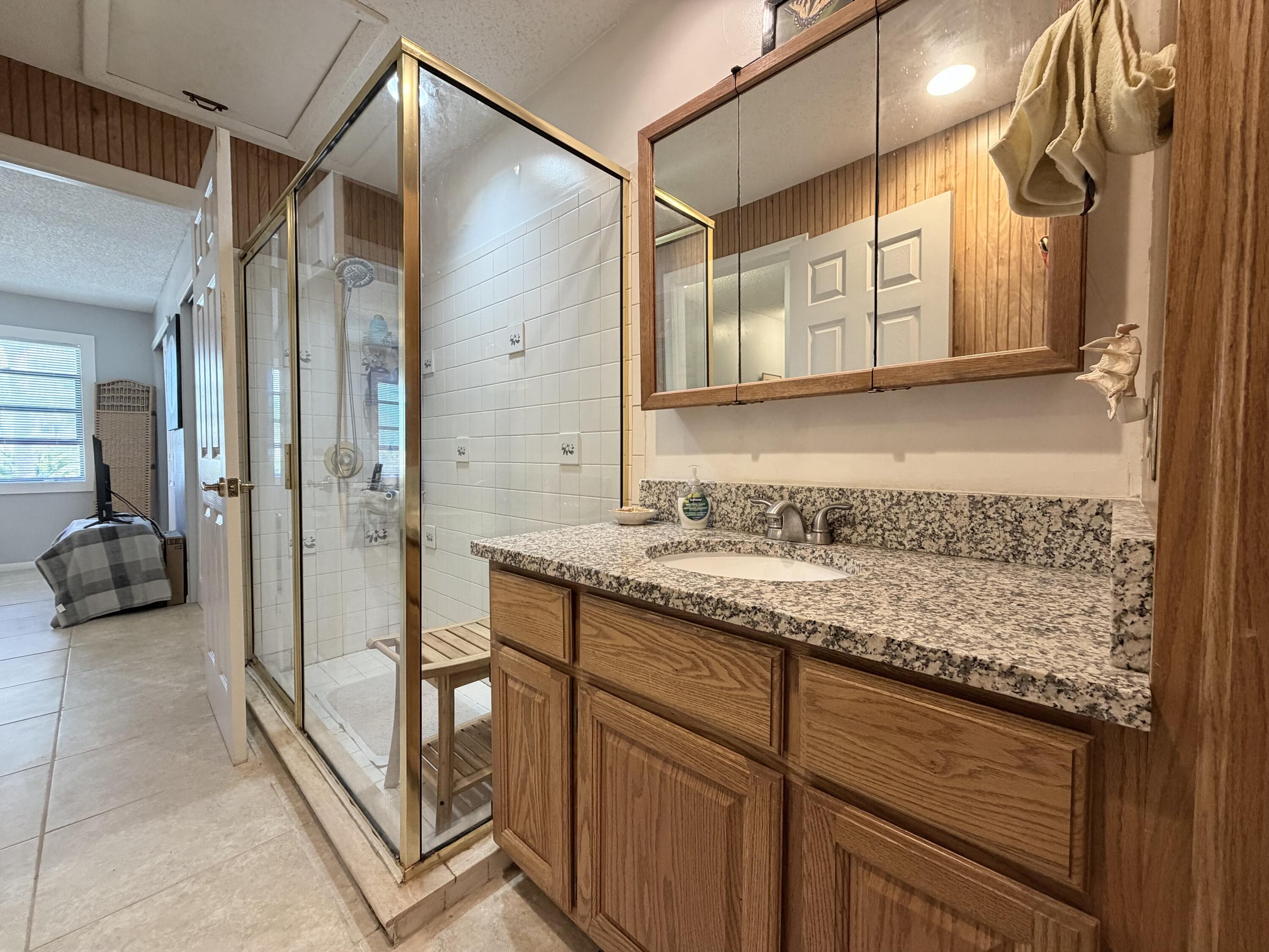 4235 North Hwy A1A, Unit 14 Hutchinson Island, FL 34949 - Photo 27 of 36 a bathroom with a granite countertop sink a mirror and a shower