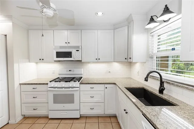 a kitchen with kitchen island granite countertop a stove a sink and dishwasher with white cabinets
