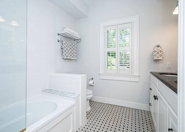 a bathroom with a granite countertop sink a toilet a window and a shower