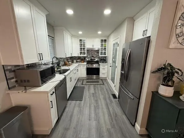 a kitchen with stainless steel appliances a refrigerator a stove a sink and white cabinets with wooden floor