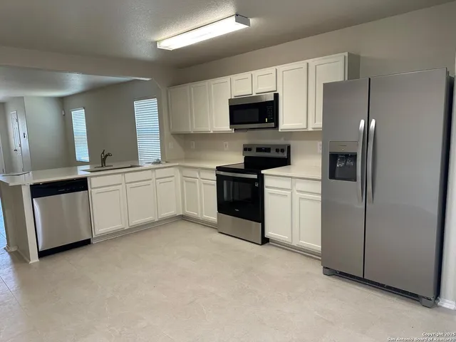 a kitchen with stainless steel appliances granite countertop white cabinets a sink a stove a microwave a refrigerator a sink and white cabinets