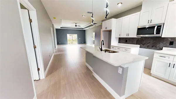 a kitchen with stainless steel appliances a white refrigerator a sink dishwasher a microwave oven a stove and white cabinets with wooden floor