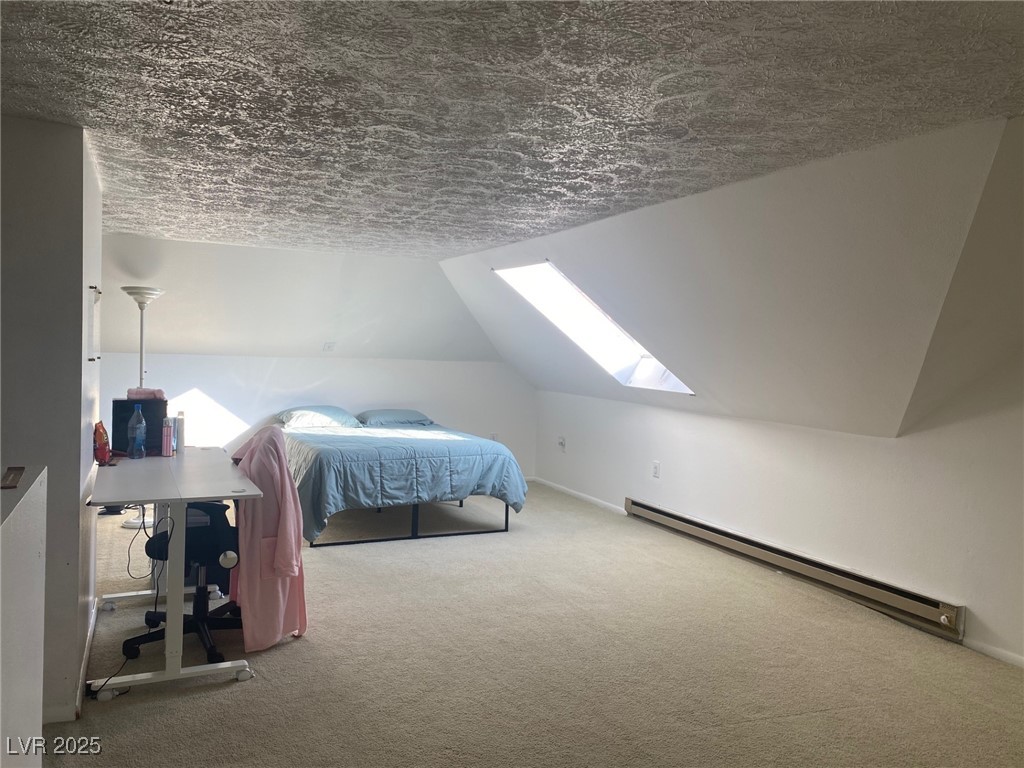 735 Canyon Street Ely, NV 89301 - Photo 12 of 20 Upstairs Bedroom with a skylight, lofted ceiling, a baseboard heating unit, carpet flooring, and a textured ceiling