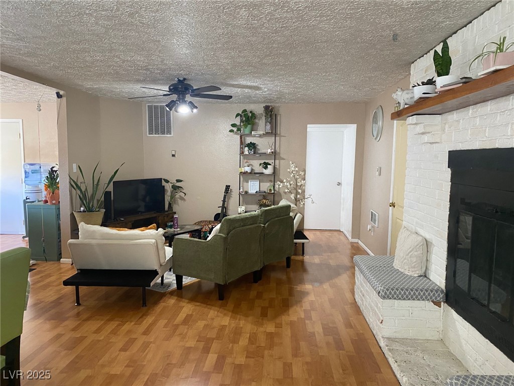 735 Canyon Street Ely, NV 89301 - Photo 2 of 19 Living area featuring a brick fireplace, a textured ceiling, wood finished floors, and a ceiling fan