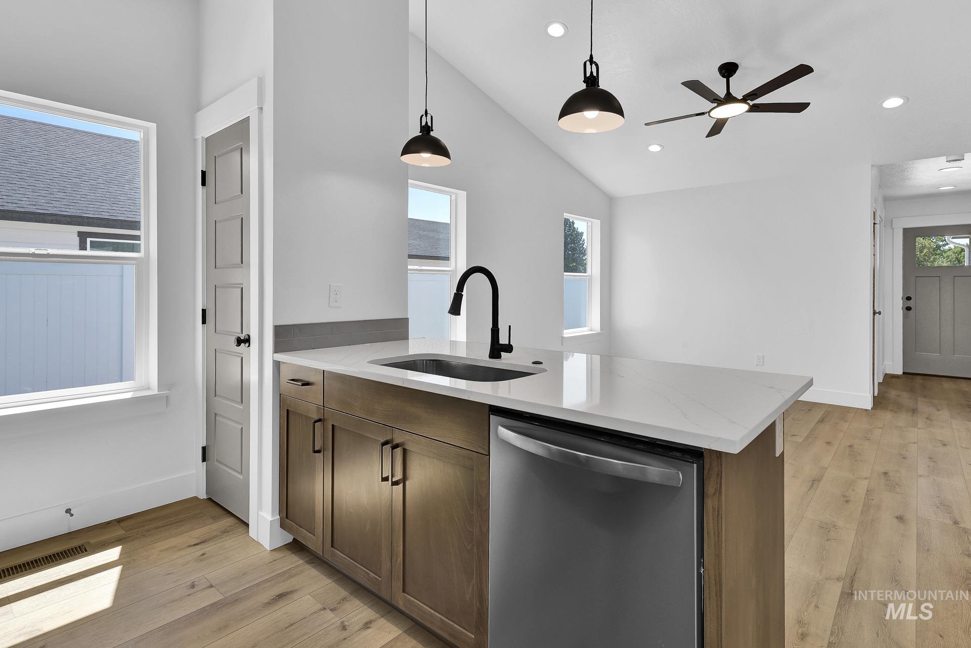 1162 Velvet Loop Wilder, ID 83676 - Photo 11 of 31 Kitchen featuring dishwasher, light stone countertops, light wood finished floors, decorative light fixtures, and a peninsula