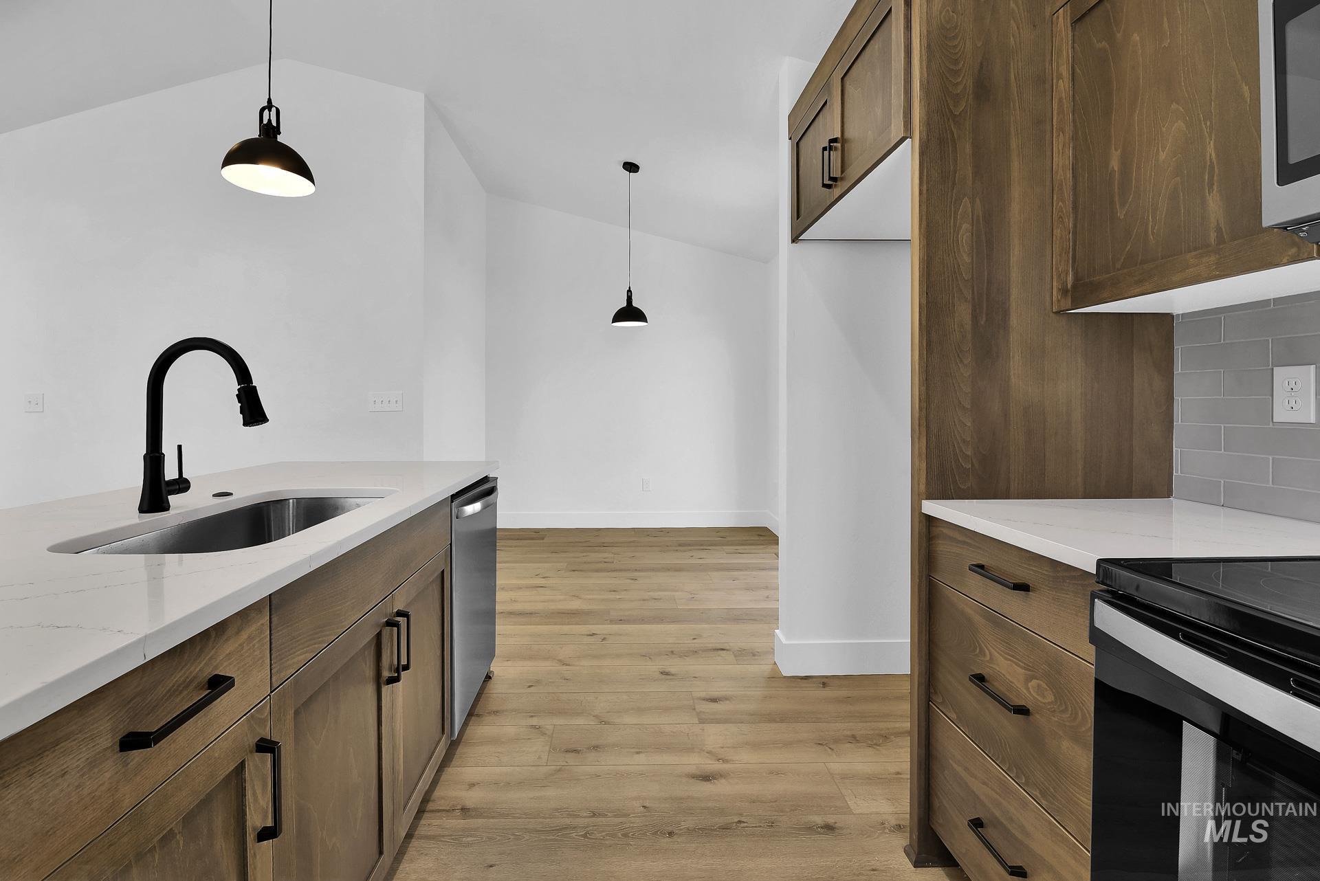 1162 Velvet Loop Wilder, ID 83676 - Photo 13 of 31 Kitchen featuring brown cabinets, light wood-style flooring, hanging light fixtures, light stone countertops, and vaulted ceiling