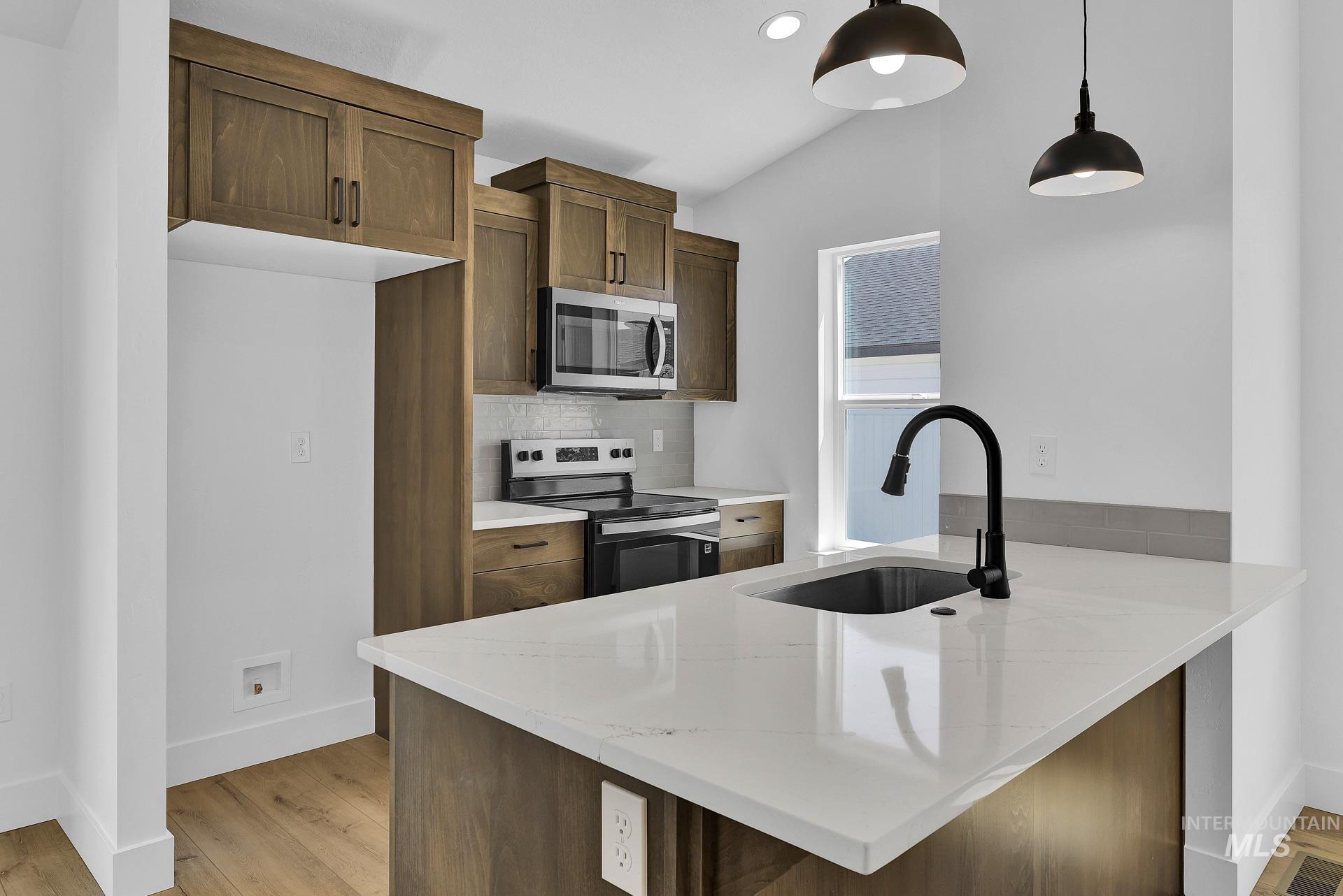 1162 Velvet Loop Wilder, ID 83676 - Photo 8 of 31 Kitchen featuring appliances with stainless steel finishes, backsplash, light wood-style flooring, a peninsula, and pendant lighting