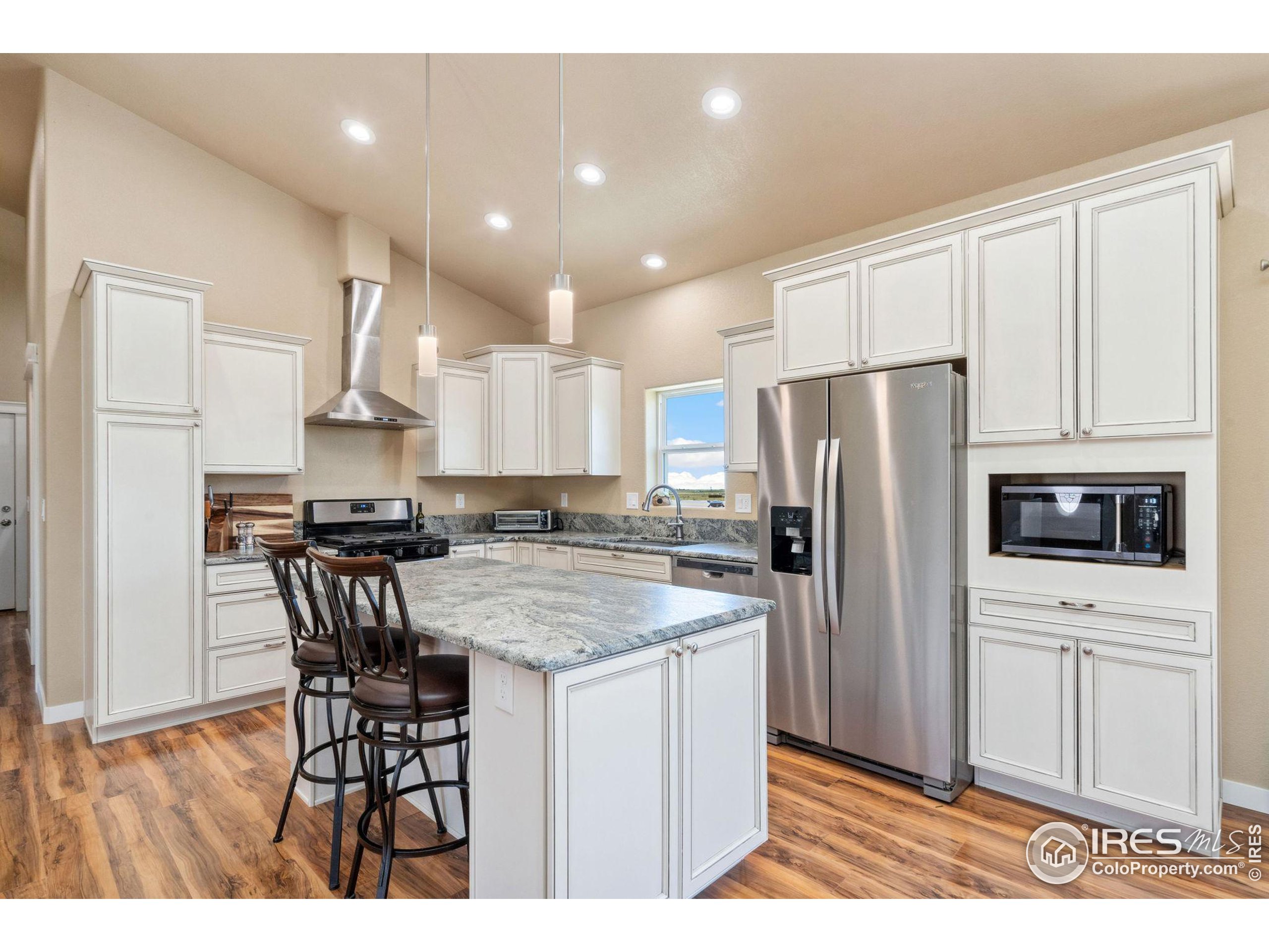 19672 Rawhide Flats Road Wellington, CO 80549 - Photo 7 of 35 a kitchen with a refrigerator a microwave a stove and white cabinets with wooden floor
