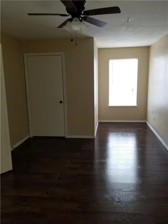 a view of an empty room with wooden floor and a ceiling fan