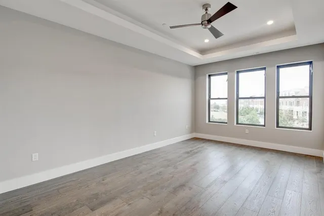an empty room with wooden floor ceiling fan and windows
