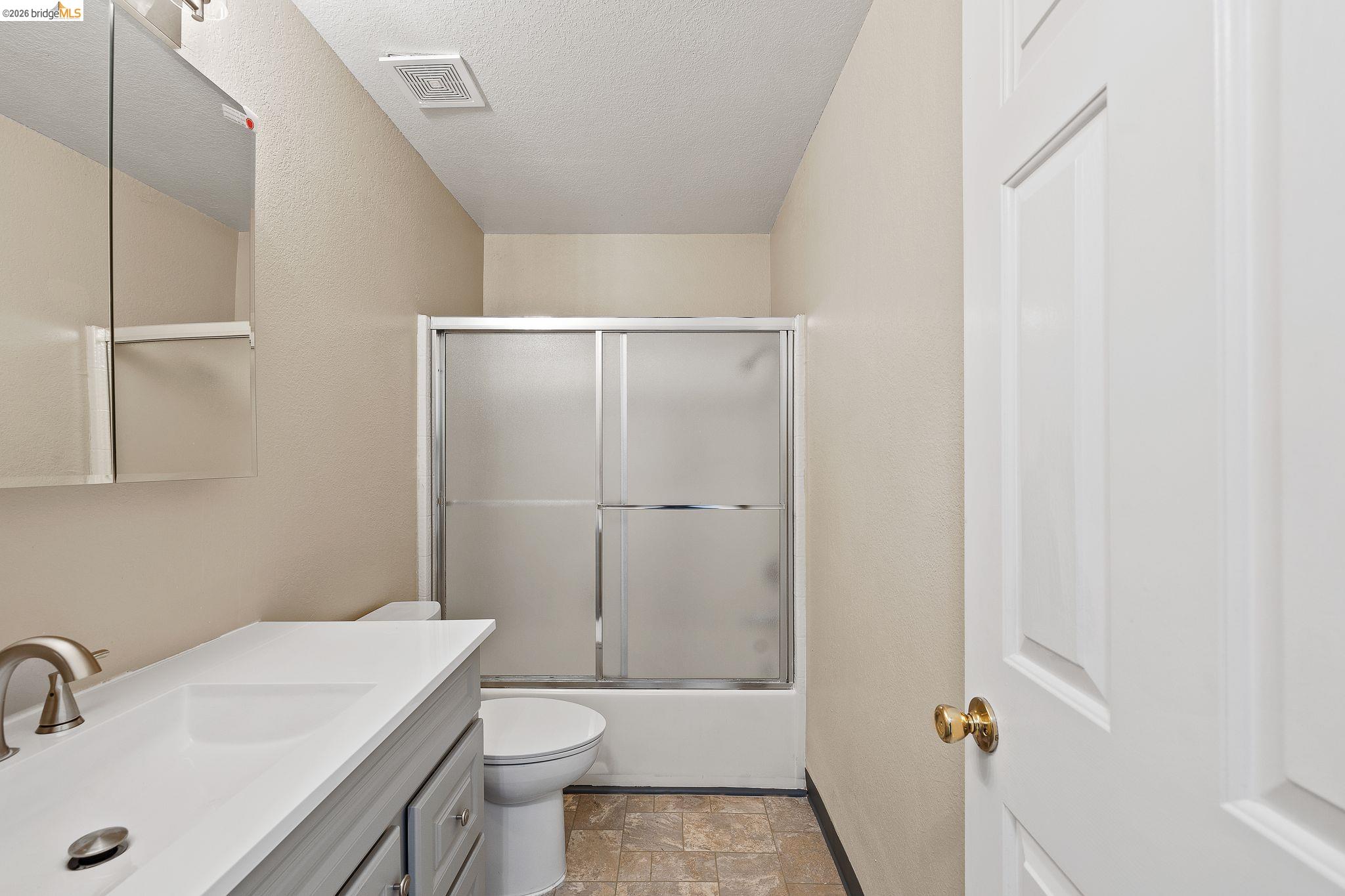 1147 Willow Lake Road Discovery Bay, CA 94505 - Photo 7 of 59 Bathroom with stone finish floors, vanity, enclosed tub / shower combo, and a textured ceiling
