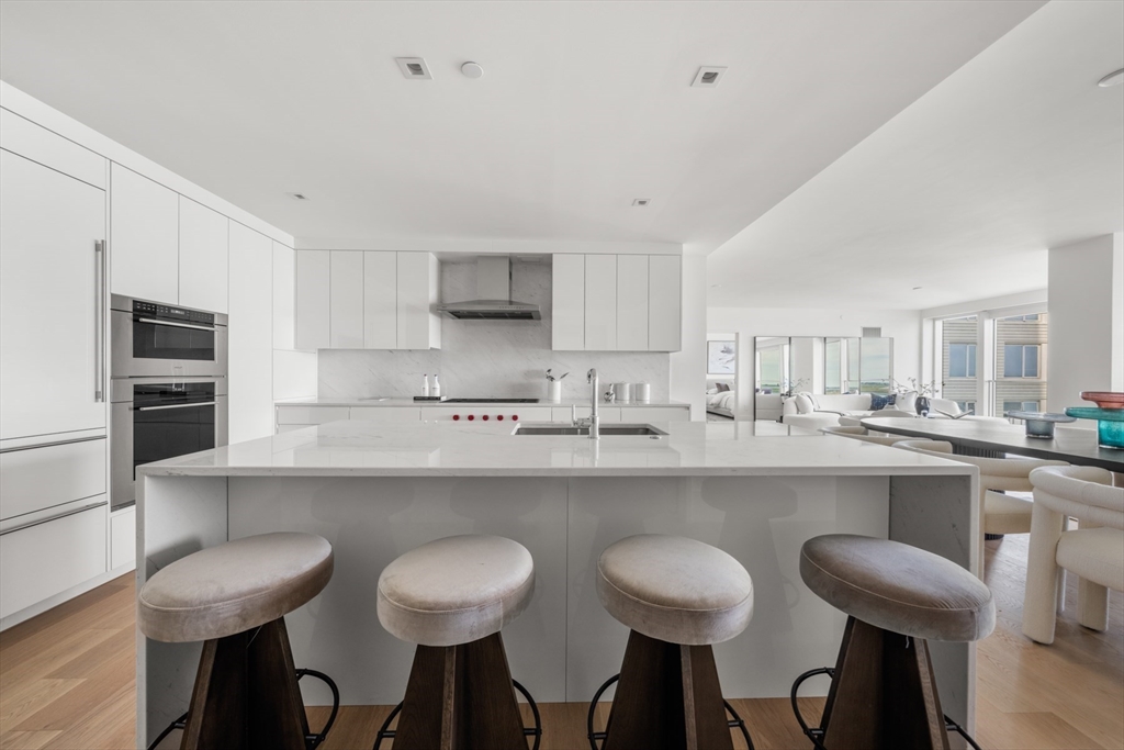 150 Seaport Boulevard, Unit 15CD Boston, MA 02210 - Photo 14 of 39 a kitchen with cabinets a sink dishwasher a stove and chairs with wooden floor