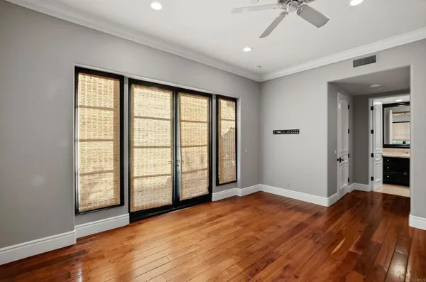 a view of an empty room with wooden floor and a ceiling fan
