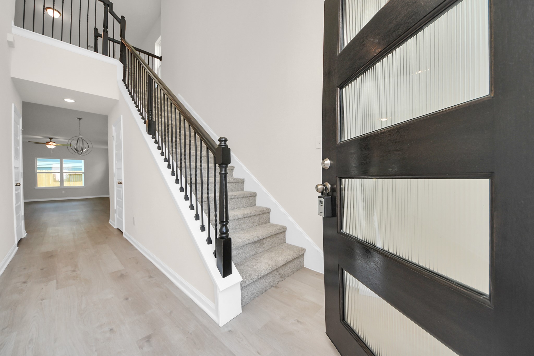 15523 Fathom Line Way Houston, TX 77053 - Photo 4 of 39 Welcome to a modern entryway featuring a sleek front door with frosted glass panels, leading into a bright hallway. The space showcases a stylish staircase with dark railings, offering a glimpse into a spacious, well-lit room beyond.