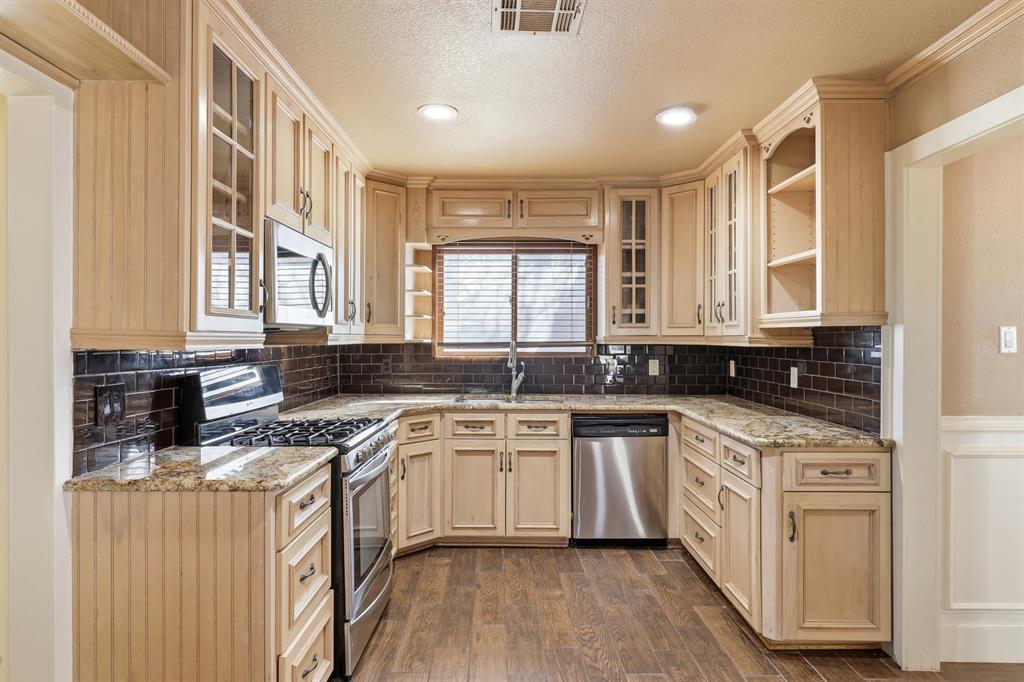 809 Cardinal Circle Bedford, TX 76022 - Photo 9 of 40 Kitchen with stainless appliances, gas range, cabinets to the ceiling with some glass cabinets, and granite countertops.