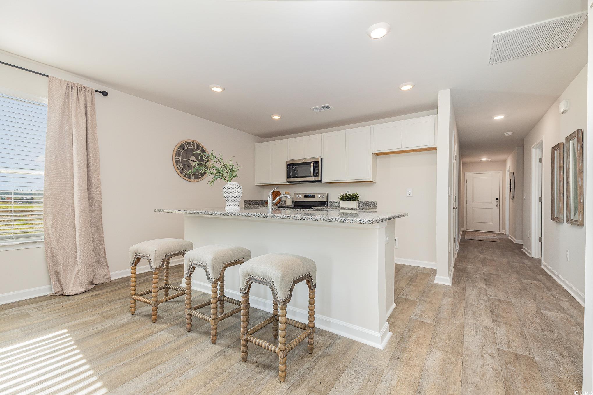 866 Farmers Passage Loop Loris, SC 29569 - Photo 3 of 25 Kitchen featuring stainless steel appliances, light wood finished floors, white cabinetry, light stone countertops, and a kitchen bar