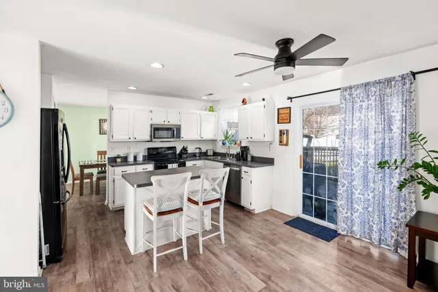 a kitchen with stainless steel appliances kitchen island granite countertop a refrigerator a stove top oven a dining table and chairs with wooden floor