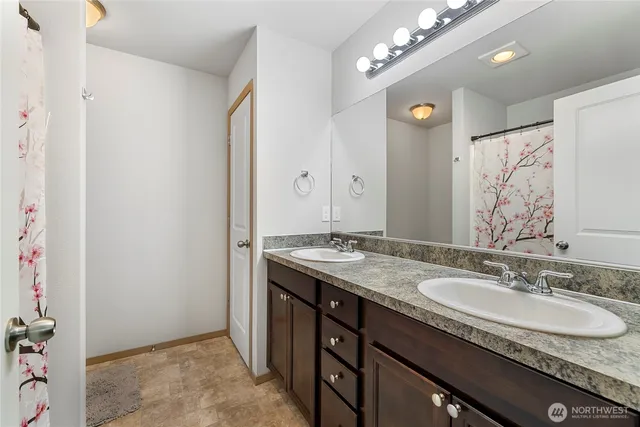 a bathroom with a granite countertop double vanity sink a mirror and a shower