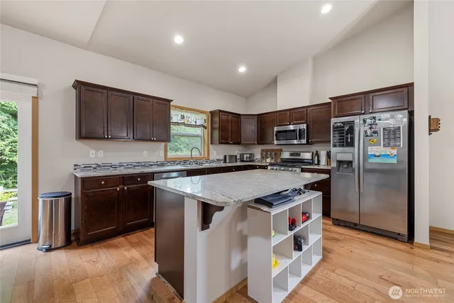 a kitchen with stainless steel appliances granite countertop a stove top oven a sink dishwasher a refrigerator and a oven with wooden floor