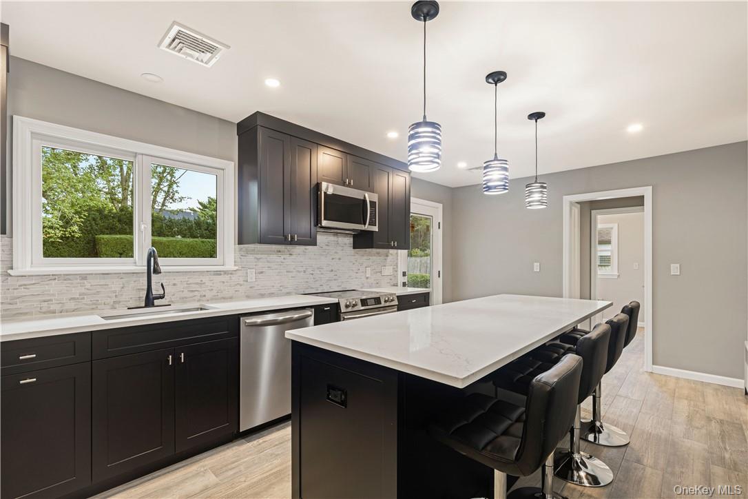5 Paddock Road Rye Brook, NY 10573 - Photo 6 of 23 Kitchen with stainless steel finishes, hanging light fixtures, a center island, decorative backsplash, door to yard