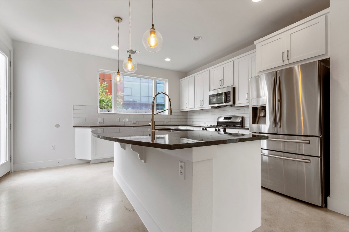 1145 Shady Lane, Unit 1A Austin, TX 78721 - Photo 19 of 25 Sleek white kitchen with large island, stainless steel appliances, and pendant lighting.