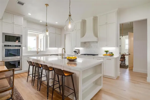 a kitchen with stainless steel appliances granite countertop a stove a refrigerator a kitchen island a sink and white cabinets with wooden floor