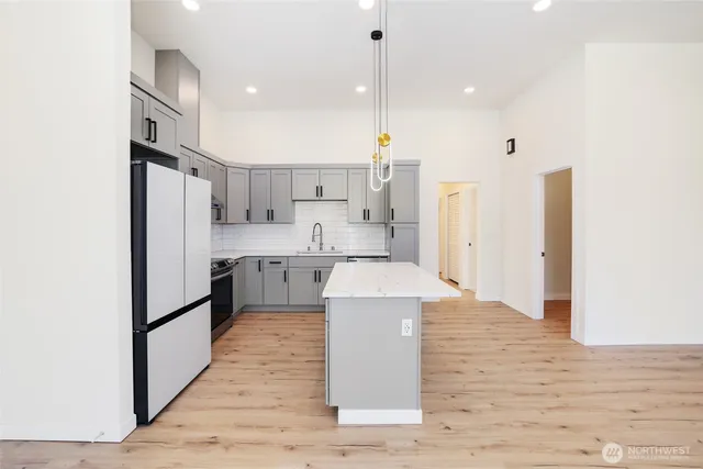 a large kitchen with stainless steel appliances granite countertop a refrigerator a sink dishwasher a oven and a dining table with wooden floor