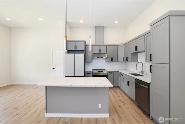 a large kitchen with stainless steel appliances granite countertop a stove a sink a refrigerator and white cabinets with wooden floor