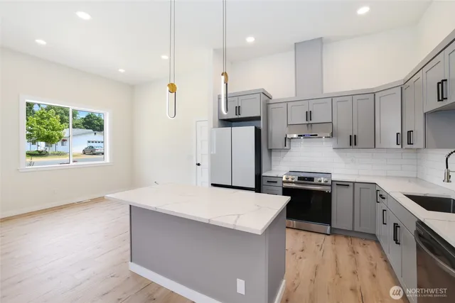 a kitchen with stainless steel appliances granite countertop a stove a refrigerator a sink a oven and a dining table with wooden floor