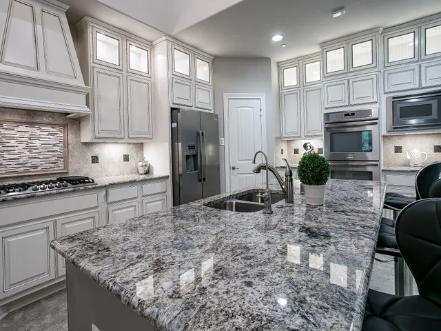 a kitchen with stainless steel appliances granite countertop a stove a refrigerator a sink a oven with white cabinets and wooden floor