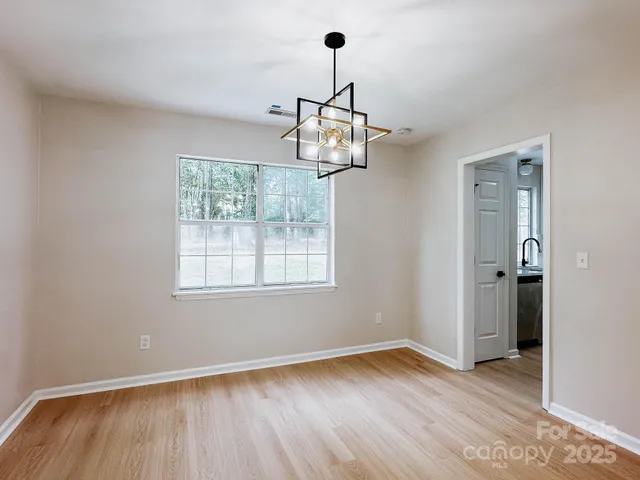 an empty room with wooden floor chandelier and windows