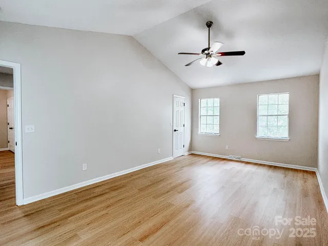 an empty room with wooden floor ceiling fan and windows