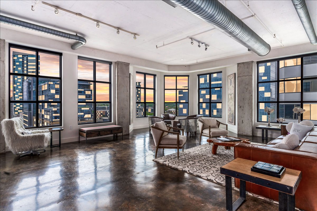 This expansive living room showcases floor-to-ceiling windows framing city views, while natural light fills the open space, creating a bright, sophisticated setting for elevated urban living.