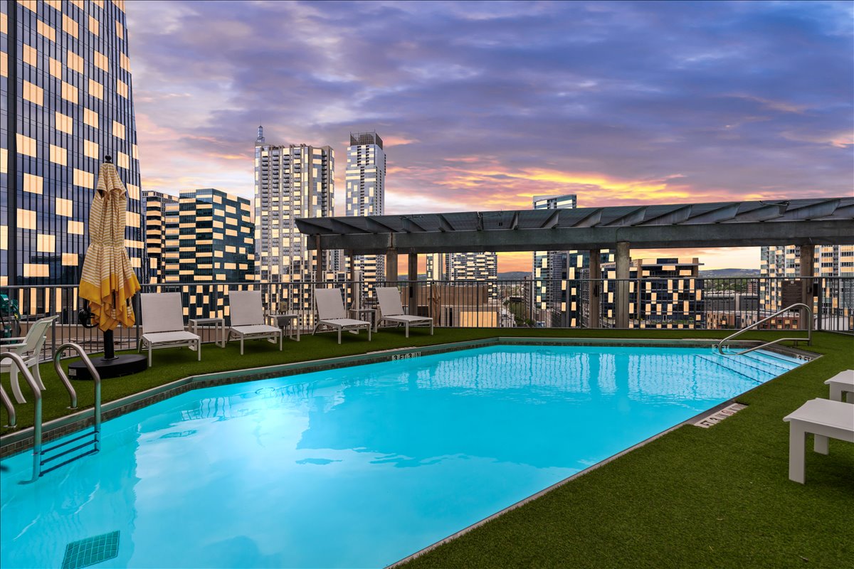 311 West 5th Street, Unit 1005 Austin, TX 78701 - Photo 28 of 30 An expansive, resort-style pool invites relaxation, while comfortable lounge seating and soft evening light create a serene, sophisticated retreat at dusk.