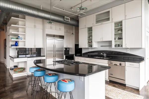 a kitchen with stainless steel appliances granite countertop a stove a refrigerator a sink and white cabinets with wooden floor