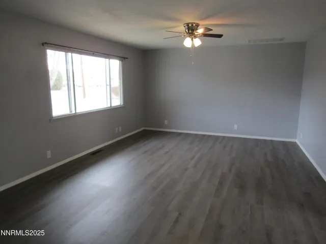 an empty room with wooden floor chandelier fan and windows