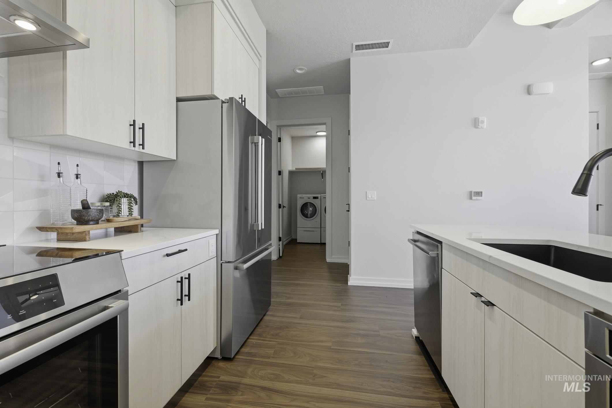 4250 East Haystack Street, Unit 308 Boise, ID 83716 - Photo 8 of 27 Kitchen featuring stainless steel appliances, dark wood-style floors, white cabinets, washer / dryer, and light stone counters