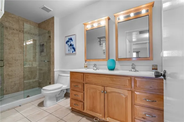 a spacious bathroom with double sink a toilet a mirror and shower
