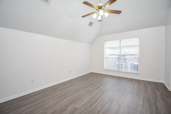 an empty room with wooden floor fan and windows