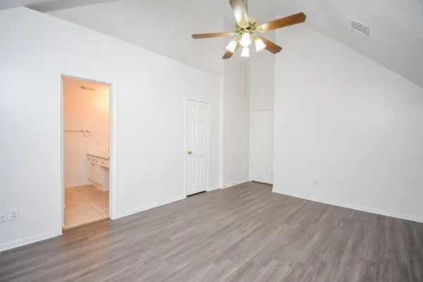 an empty room with wooden floor fan and windows