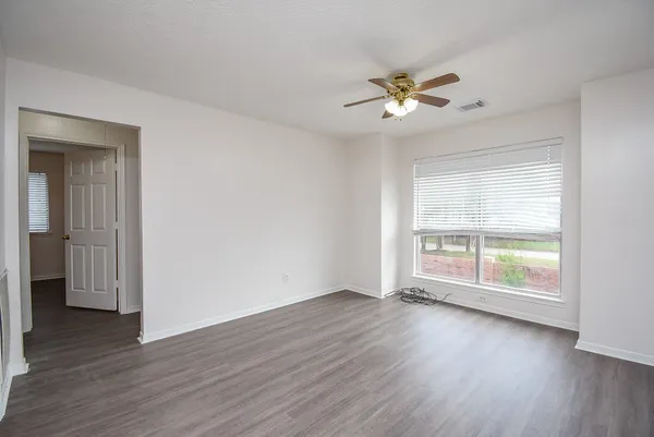 an empty room with wooden floor fan and windows